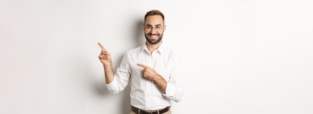 Free photo handsome successful businessman pointing fingers right showing advertisement with pleased face white