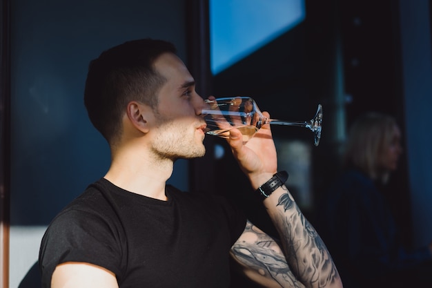 Handsome tattooed man on a summer terrace in a city cafe is drinking wine. Street Cafe.