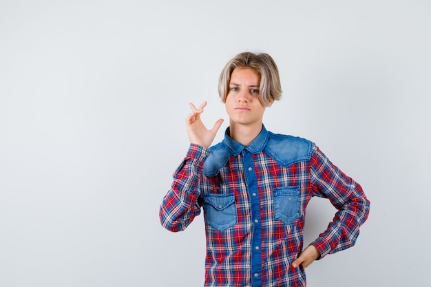 Handsome teen boy in checked shirt pointing at upper left corner and looking thoughtful , front view.