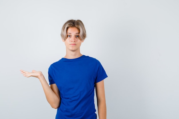 Free photo handsome teen boy pretending to hold or show something in blue t-shirt and looking puzzled , front view.