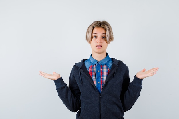 Handsome teen boy showing helpless gesture in shirt, hoodie and looking puzzled , front view.