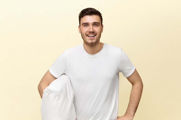 Handsome tired young man holding white pillow