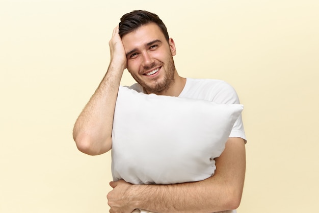 Handsome tired young man holding white pillow