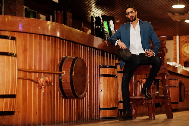 Free photo handsome welldressed arabian man with glass of whiskey and cigar posed at pub