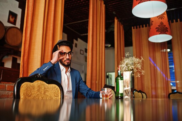 Handsome welldressed arabian man with glass of whiskey and cigar posed at pub