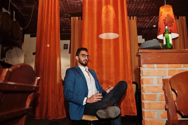 Handsome welldressed arabian man with glass of whiskey and cigar posed at pub