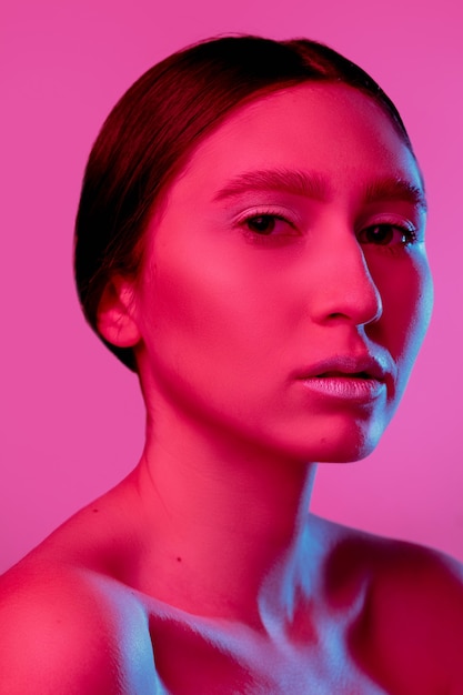 Handsome woman's portrait isolated on pink studio background in neon light, monochrome. Beautiful female model. Concept of human emotions, facial expression, sales, ad, fashion and beauty.