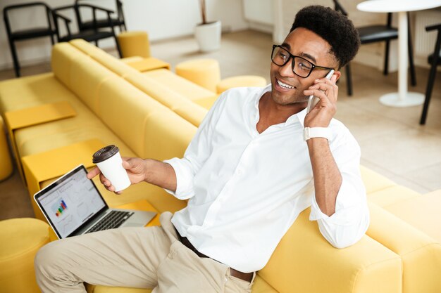 Handsome young african man talking by phone drinking coffee.