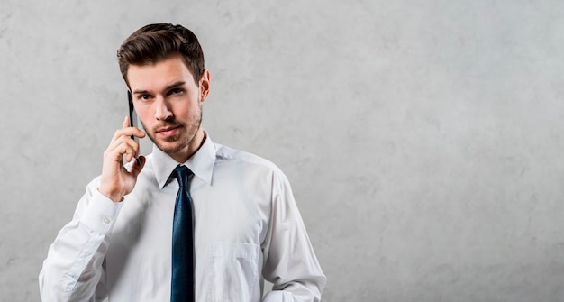 Handsome young businessman talking on mobile phone against grey wall