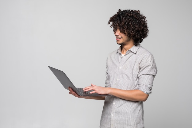 Handsome young curly haired man working on laptop computer standing of isolated on white wall,