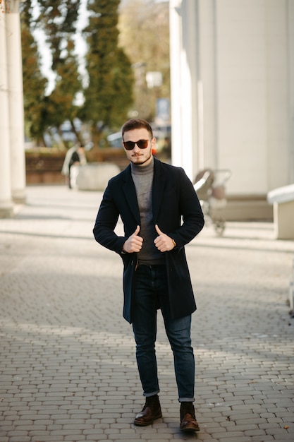 Free photo handsome young fashion model posing on city streets.outdoor fashion portrait, stylish man in elegant coat.