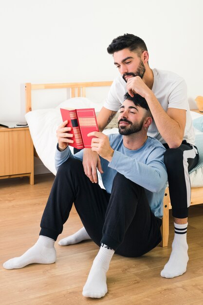 Handsome young gay couple together reading the book in the bedroom