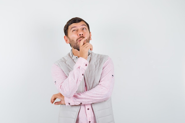 Handsome young male with hand on chin, looking up in shirt, vest and looking thoughtful , front view.