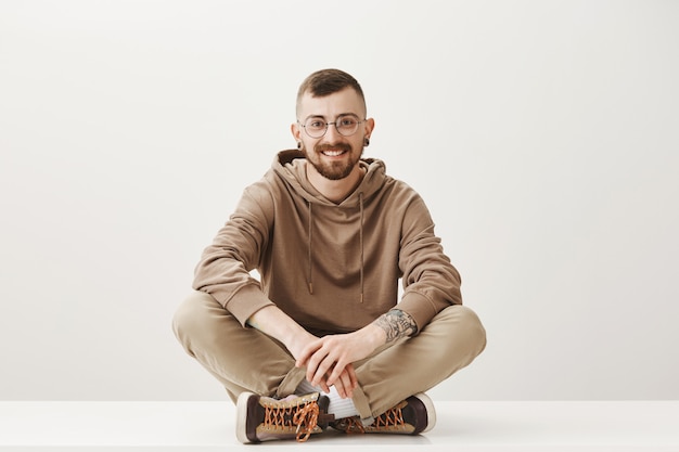 Handsome young man in glasses sitting on floor and smiling friendly