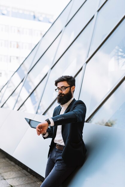 Handsome young man holding digital tablet watching time on wrist watch