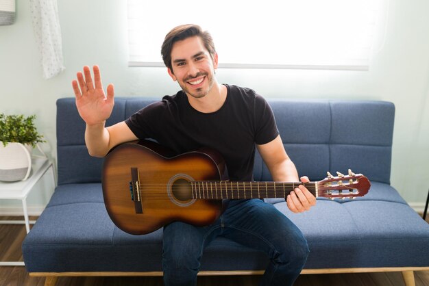 Handsome young man playing the acoustic guitar while smiling and making eye contact. Male music teacher ready for his student during an online class