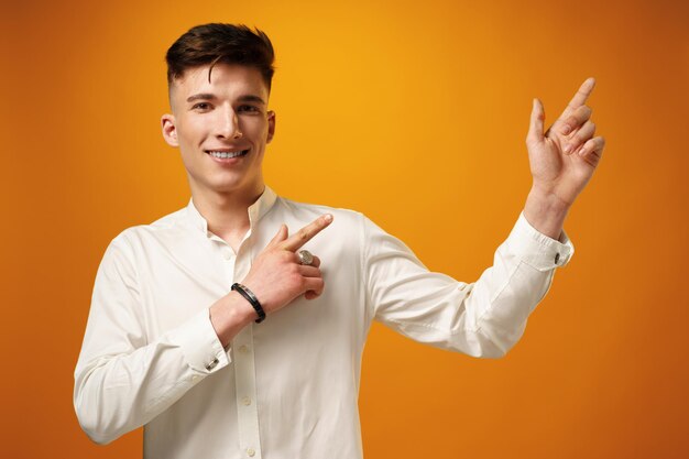 Handsome young man pointing copy space against yellow background