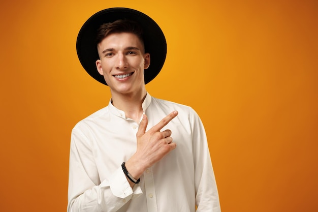 Handsome young man pointing copy space against yellow background