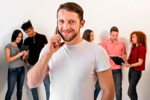 Handsome young man talking on cellphone against his friends at background