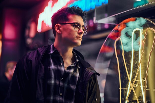 A handsome young man wearing sports hoodie standing in the street at night. Illuminated signboards, neon, lights.