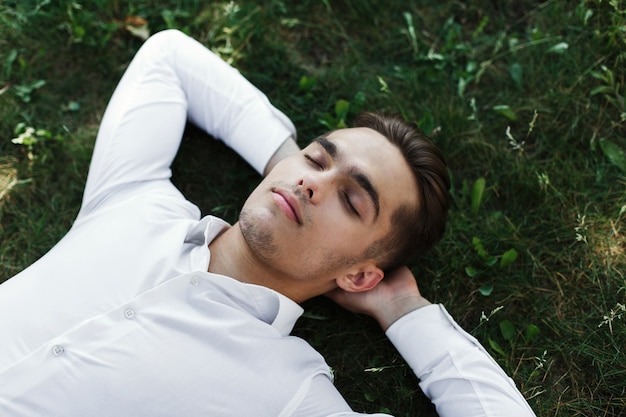 Handsome young man in a white shirt lies on the ground