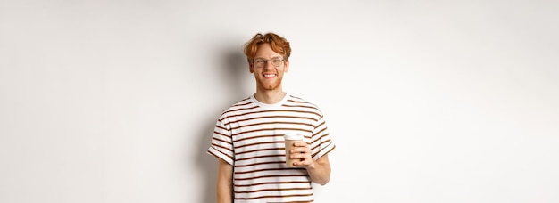 Free photo handsome young man with beard and red messy hair wearing glasses with striped tshirt drinking coffee