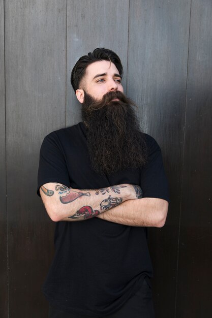 Handsome young man with standing in front of wooden black wall with arms crossed