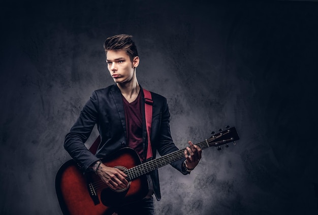 Free photo handsome young musician with stylish hair in elegant clothes with a guitar in his hands playing and posing on a dark background.