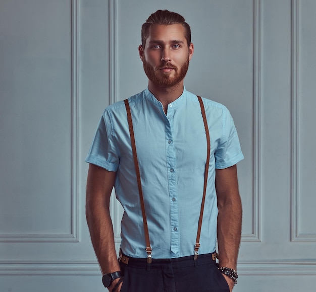 Free Photo a handsome young retro stylish redhead man in suspenders posing against a white wall in a studio.