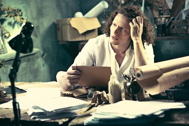 Free photo handsome young writer sitting at the table and writing something in his sketchpad at home