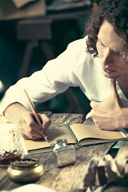 Free Photo handsome young writer sitting at the table and writing something in his sketchpad at home