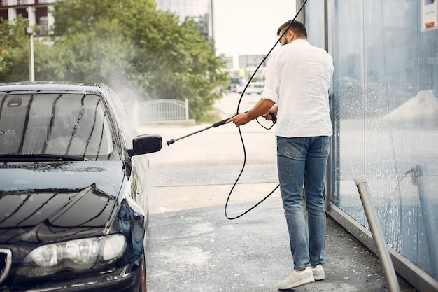 Handsomen man in a white shirt washing his car 