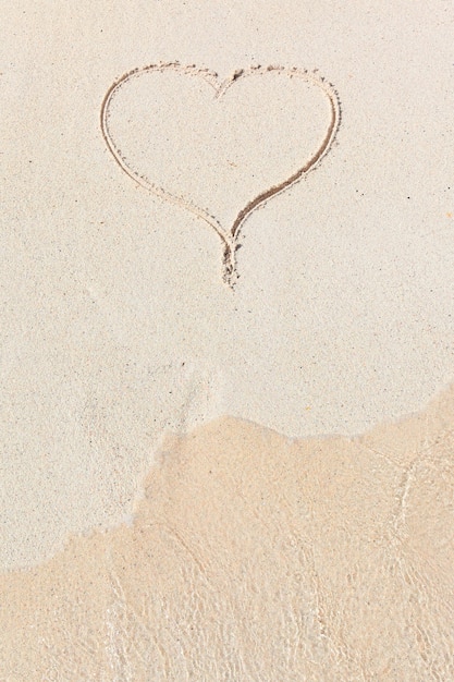 Free photo handwritten heart in sand with wave approaching in the beach