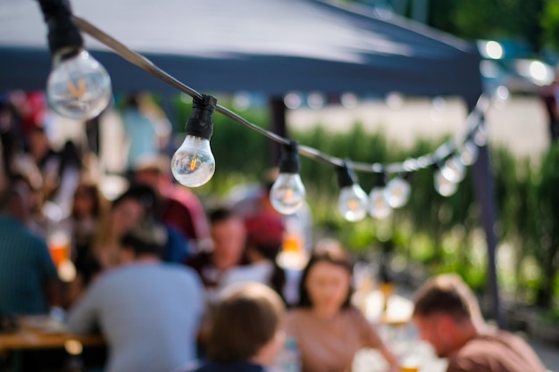 Free Photo hanged lamps at outdoor restaurant with multiple visitors on the background, bbq