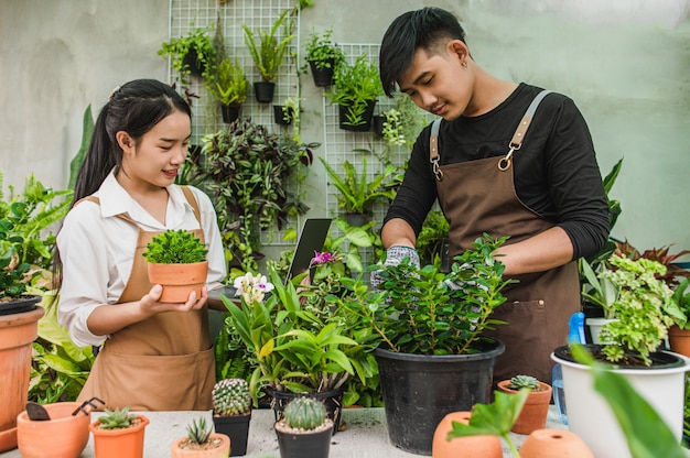 Happily Asian young gardener couple wearing apron use garden equipment and laptop computer to take care