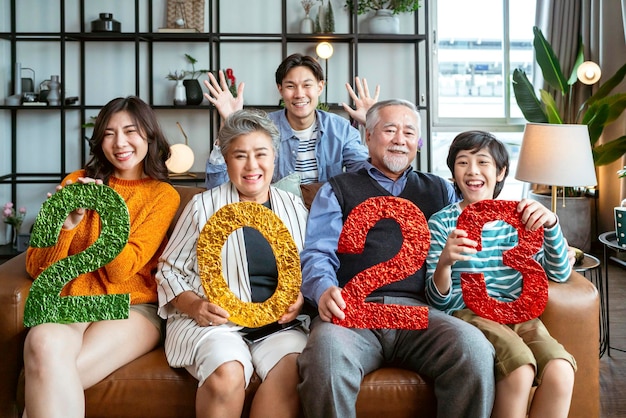 Happiness asian multi generation 2023 new year celebrateasian family hold 2023 text number on sofa at living room with laugh smile cheerful moment togethergrandparent grandson parent sit relax sofa