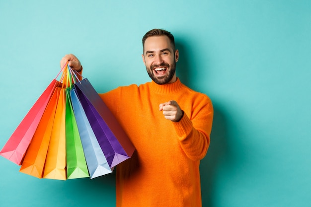 Happy adult man pointing finger at camera, holding shopping bags and smiling