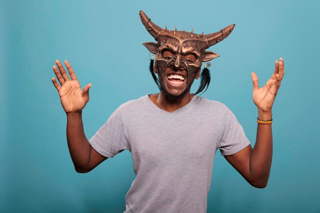 Happy adult wearing tribal native ceremonial face mask used in indigenous culture and history to create ancient ritual. African american guy with traditional and cultural shaman object.