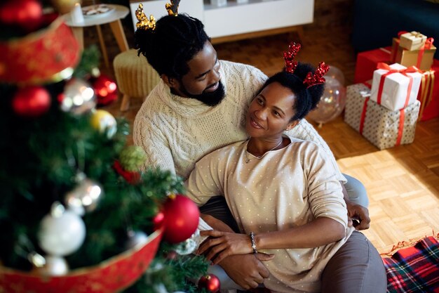 Happy African American couple relaxing by Christmas tree at home