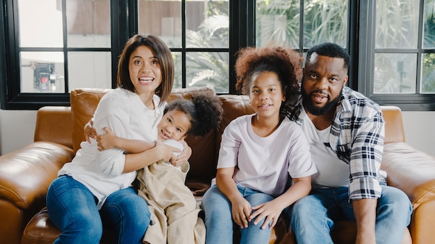 Happy African American family dad, mom and daughter having fun cuddle and video call on laptop on sofa at house.