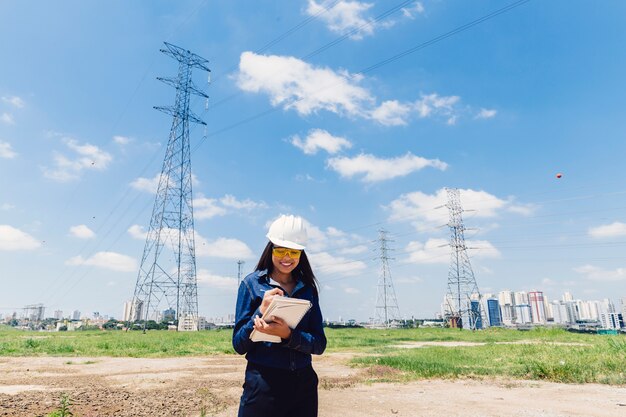 Happy African American lady in safety helmet taking notes near high voltage line