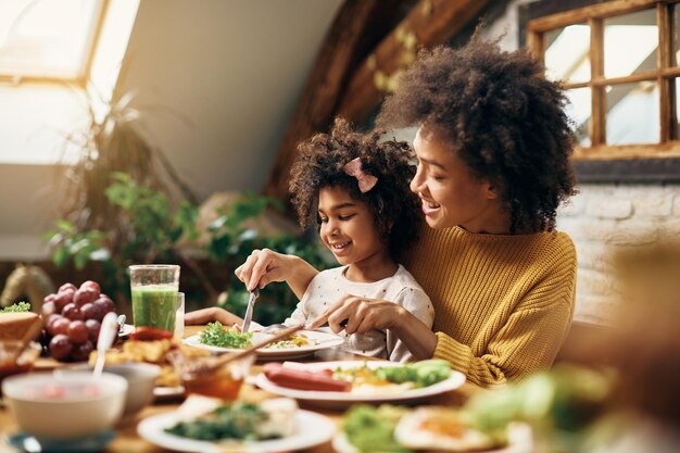 Happy African American mother and daughter eating at dining table