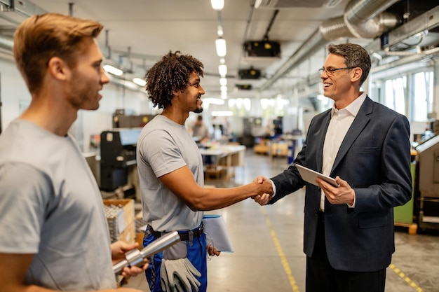 Happy African American worker greeting with quality control inspector in industrial building