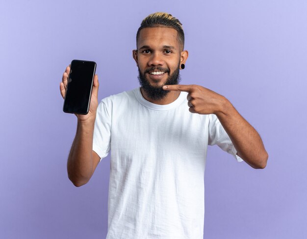 Happy african american young man in white t-shirt showing smartphone pointing