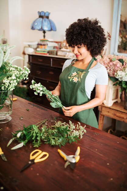 Happy african female florist looking at bunch of white flowers in shop