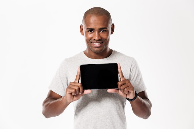 Happy african man showing blank tablet computer screen and looking