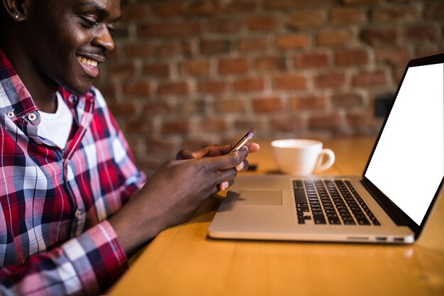 Happy Afro American college student with cute smile typing text message on electronic gadget, sitting at cafe tablein cafe.