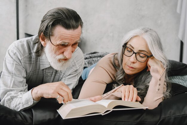 Happy aged married couple relaxing together at home. Senior couple reading book on bed.