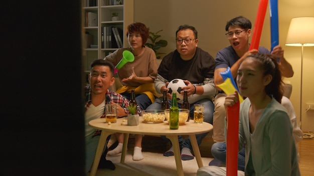 Happy asian friends or football fans watching soccer on tv and celebrating victory at home