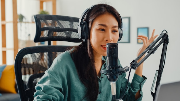 Free photo happy asian girl recording a podcast on her laptop computer with headphones and microphone